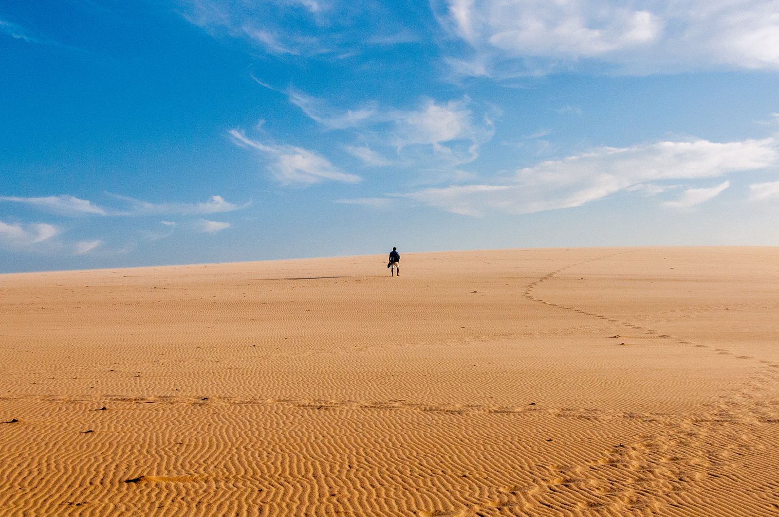 A lone walker crossing a wide, empty desert.