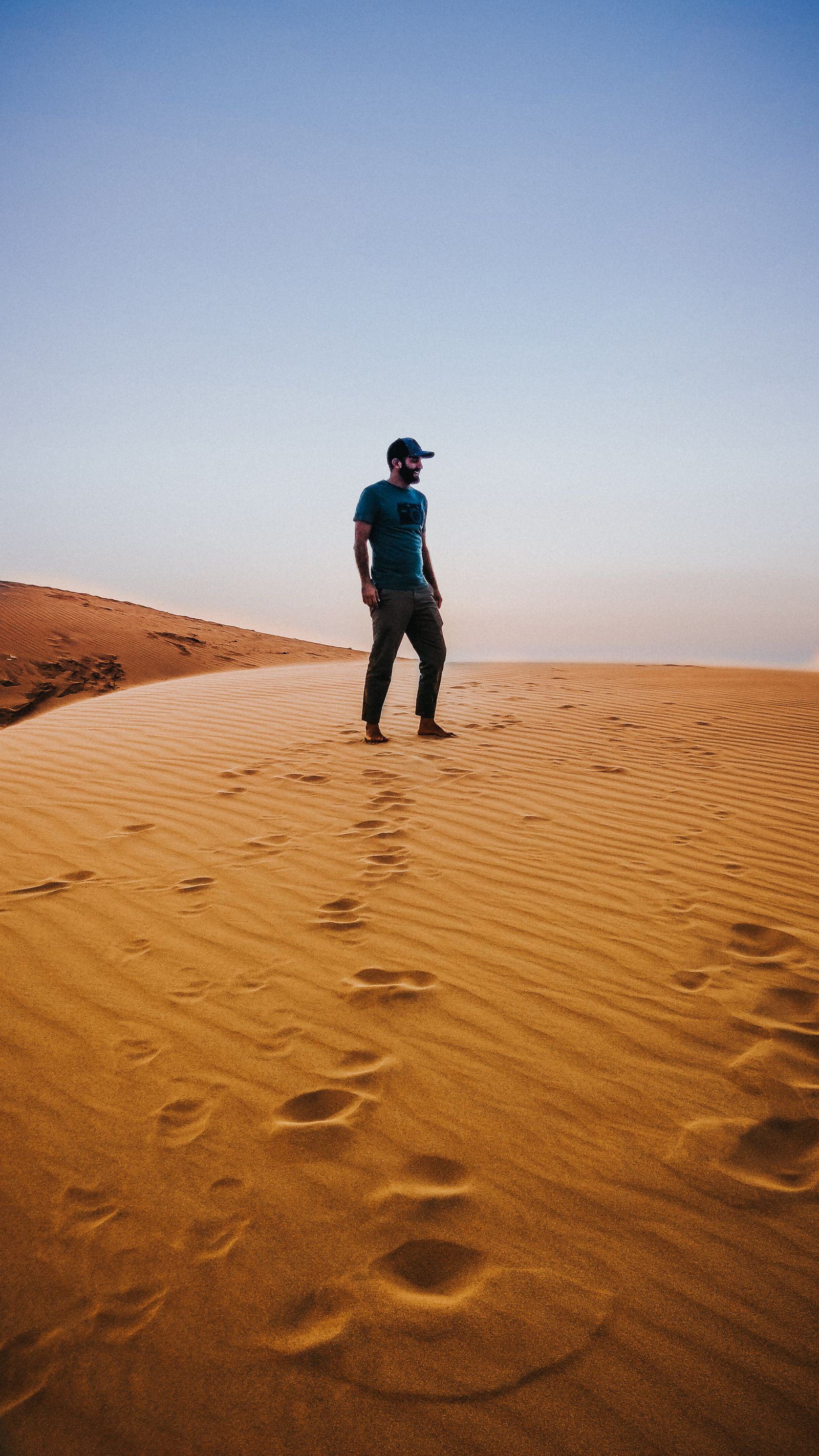A barefoot traveller standing on the crest of a dune.