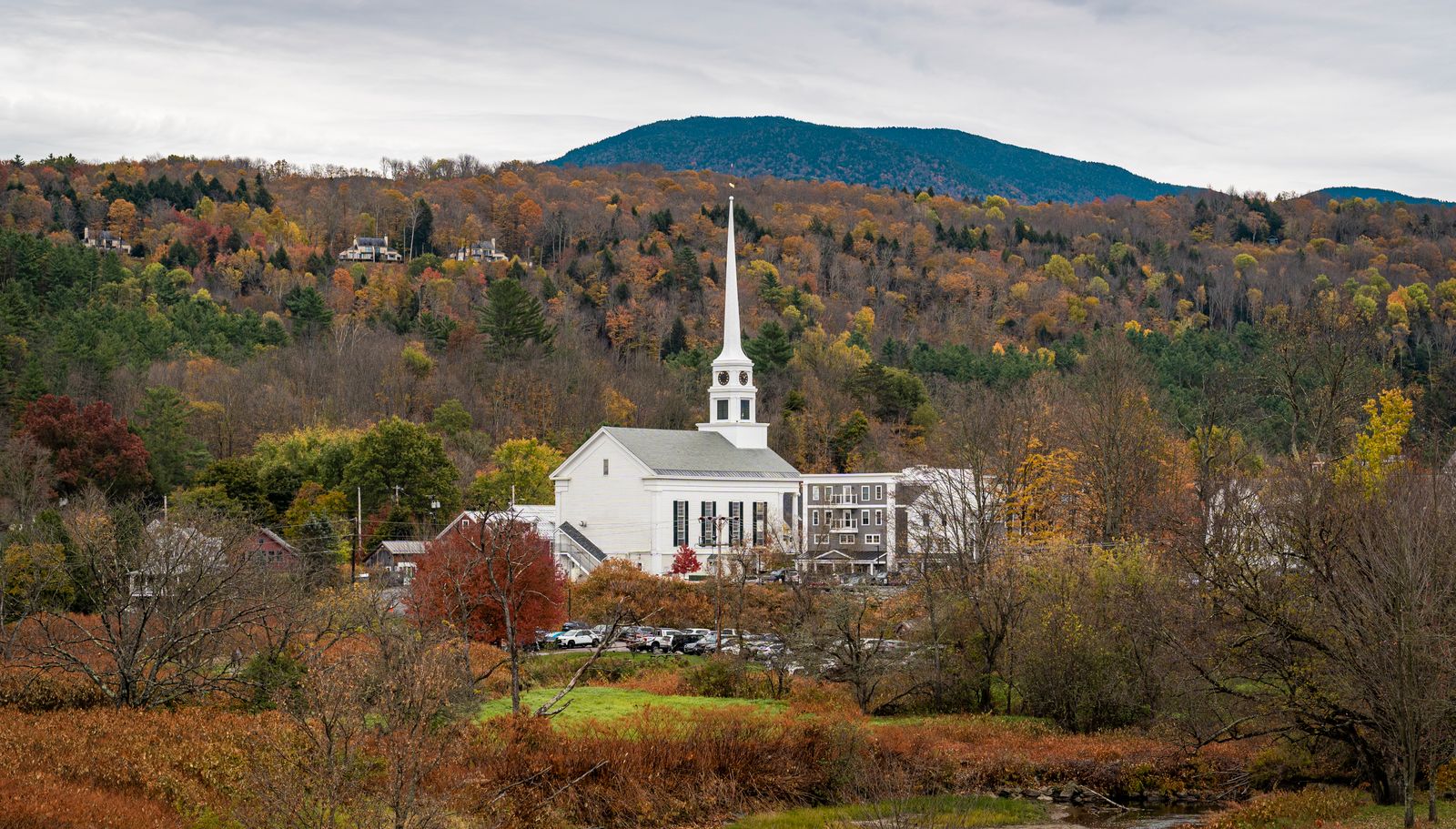 A white New England church steeple among vivid autumn foliage.