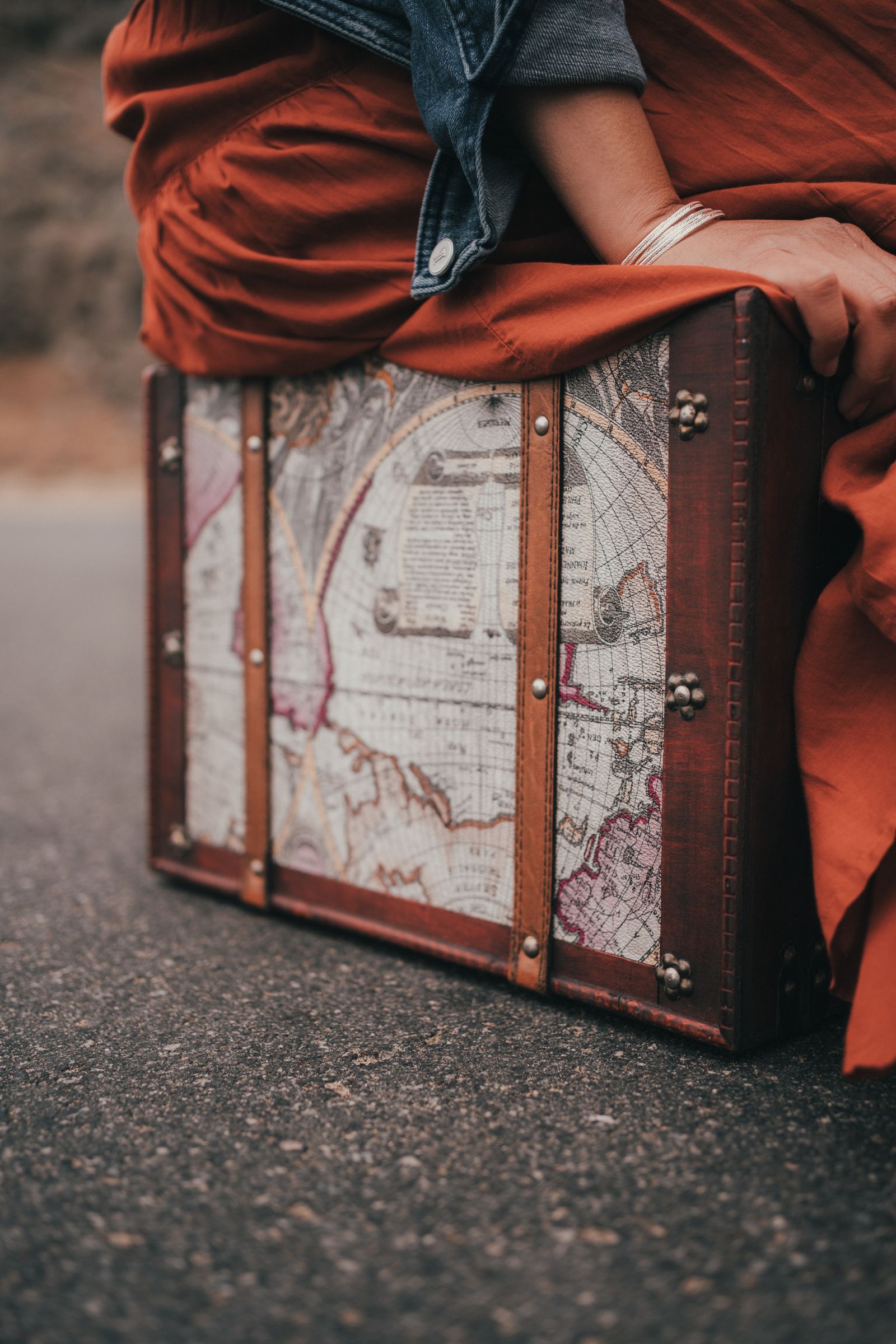 A woman sitting on a vintage suitcase printed with an old map.