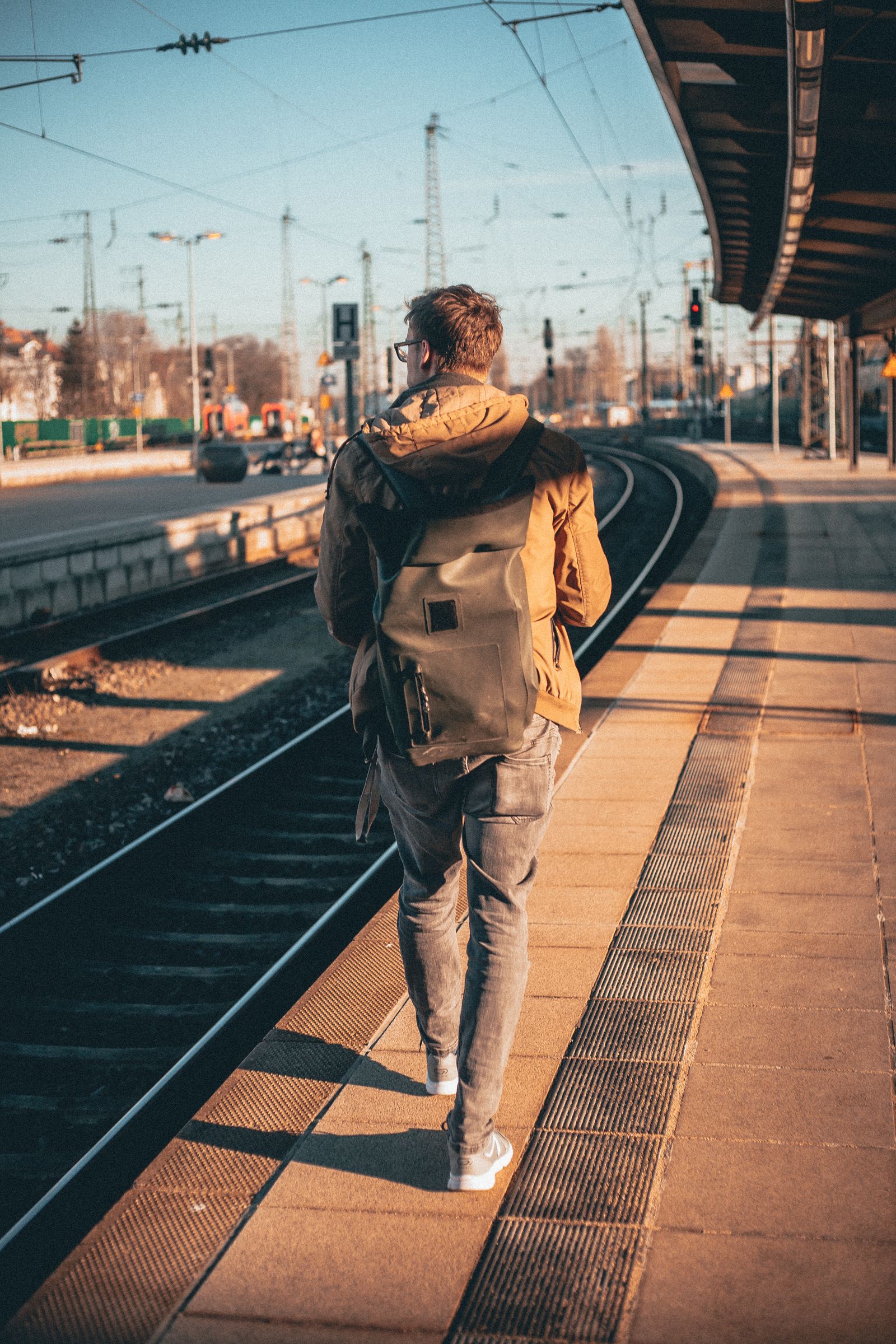 A traveller with a backpack walking along a station platform at dawn.