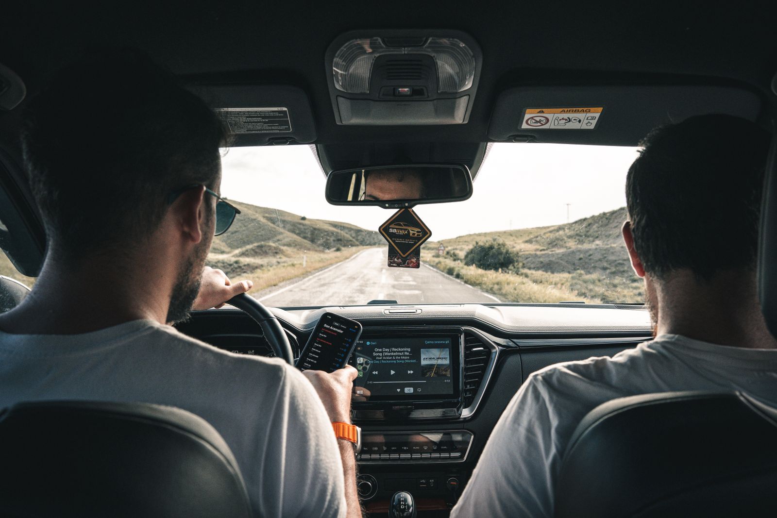 Two friends driving a coastal road, one checking the route.