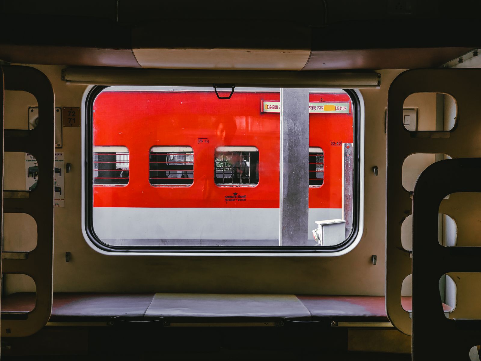 A red train seen through another train's window at a station.