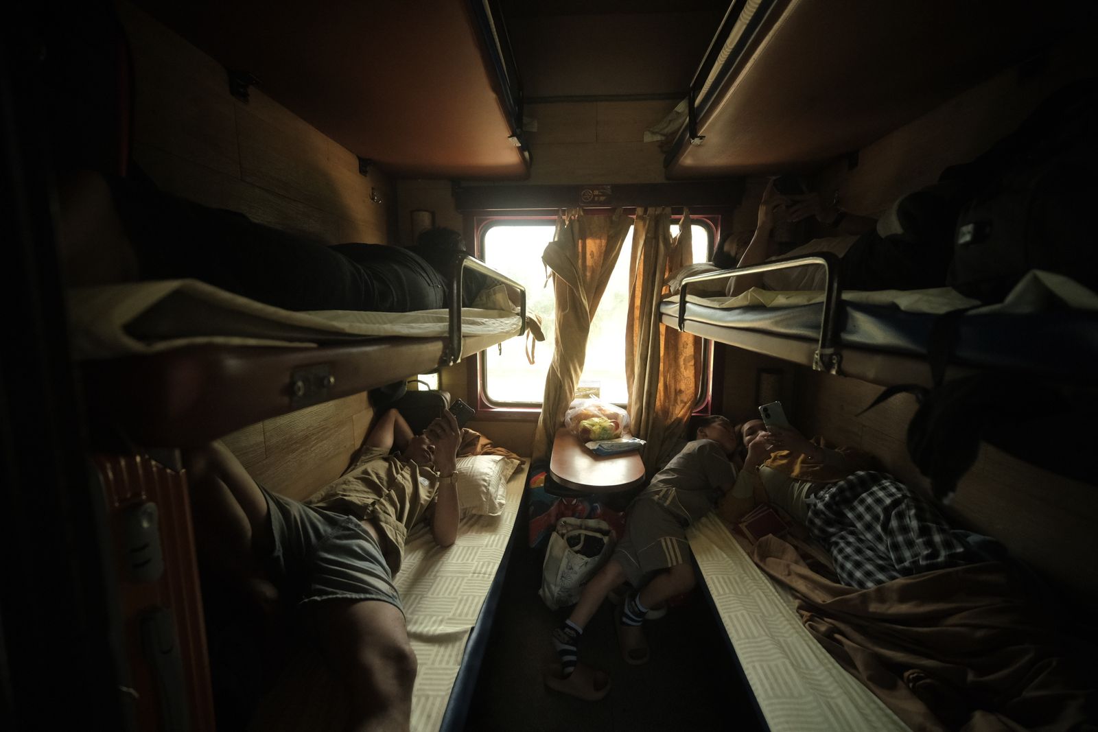 Passengers resting in a sleeper cabin with bunks and a window.